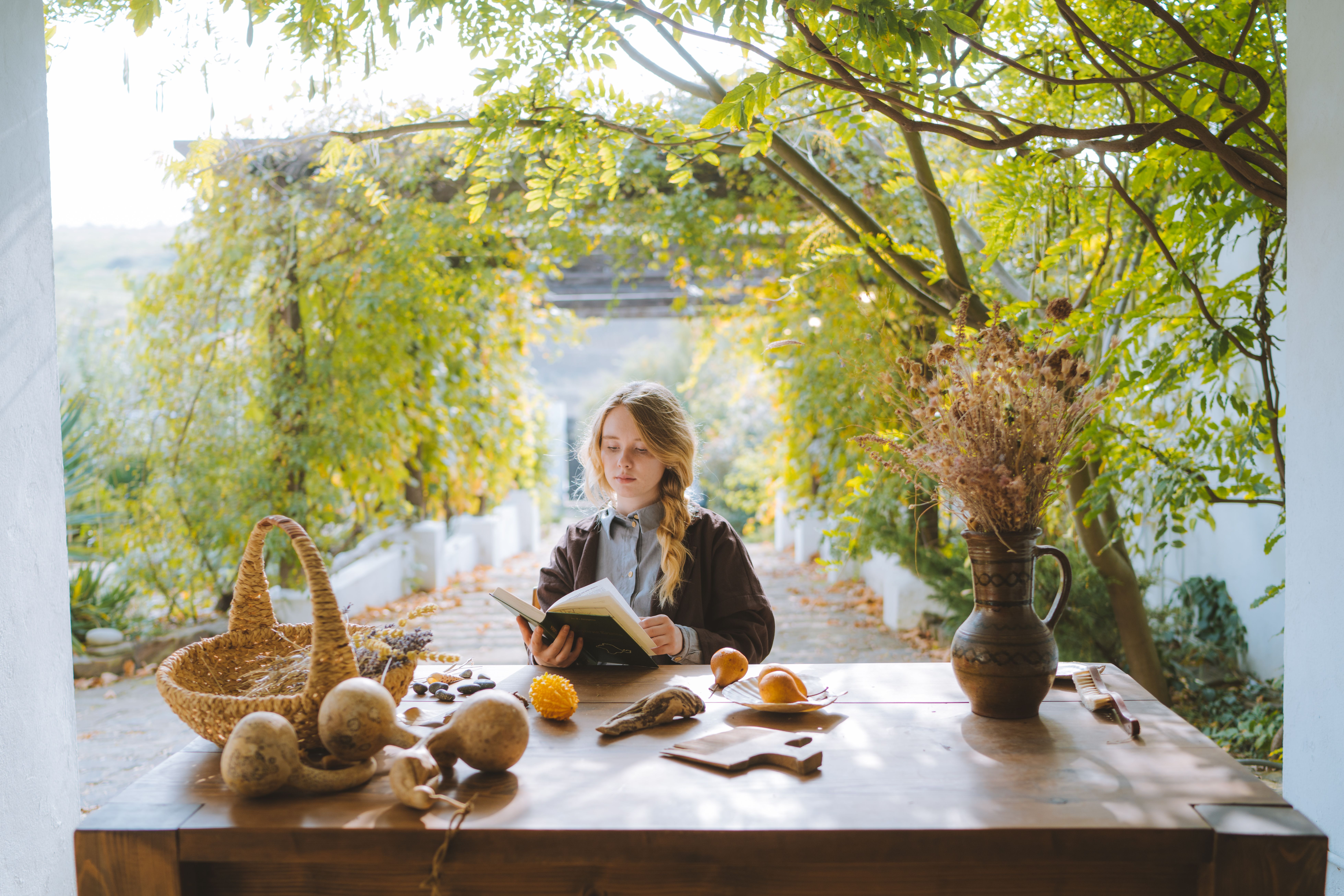 Woman reading a book at a table in a serene garden with autumn leaves